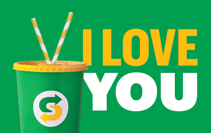 Green gift card with the text "I LOVE YOU" next to a subway cup with two white and yellow striped straws coming out of the top.