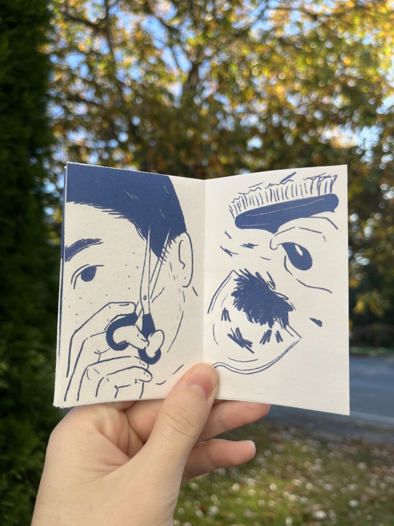 Photos of an 8 page zine held up against a blurry outdoor background. Drawings are in dark blue on a white background. Panel 6: Close-up of the person using the scissors to trim the “sideburn” hair that hangs in front of their ear. Panel 7: Overhead shot of a hand using a broom to sweep hair clippings into a dustpan.